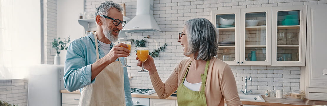 Loving senior couple in aprons toasting each other with orange juice